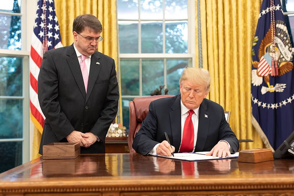 Robert Wilkie watching Donald Trump sign a bill.